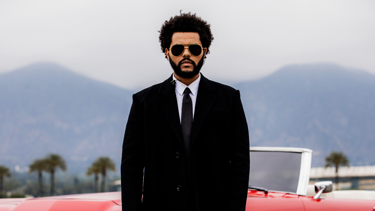 The Weeknd está prestes a lançar novo álbum. Na imagem, ele aparece de terno e gravata preto óculos escuros aviador